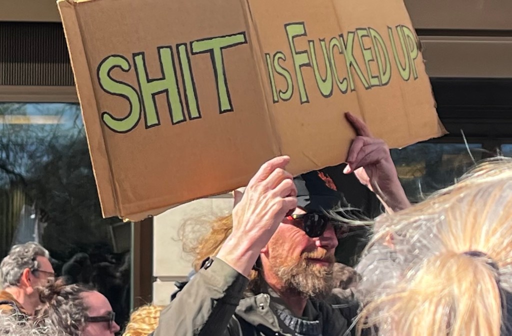 Protestor holding a sign saying "sh*t is f*cked up"